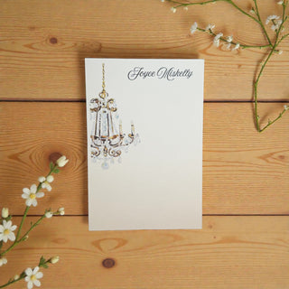 Flat note card with a chandelier illustration on a wooden surface with white flowers.
